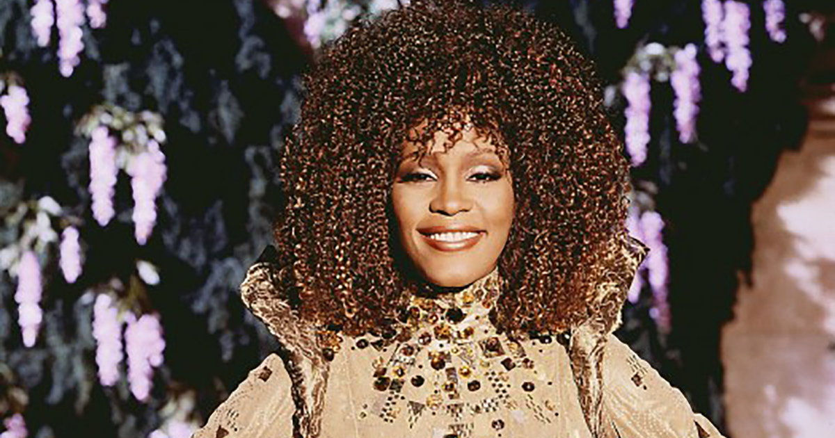 Decked out in her dazzling gold gown, Whitney Houston smiles, in character as the Fairy Godmother in 1997's Cinderella.